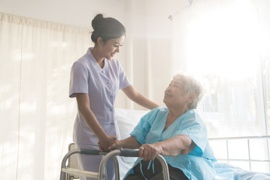 asian young nurse supporting elderly patient disabled woman in using walker in hospital. elderly patient care concept.