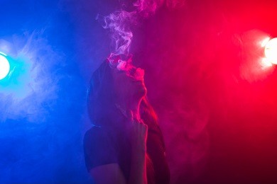 young woman in black t-shirt vaping in red and blue neon light