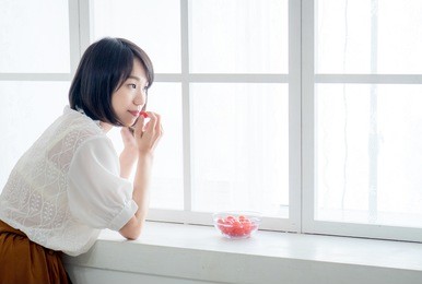 young woman enjoying tasty healthy fruit in front of window