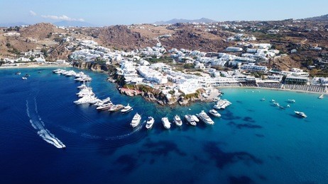 aerial drone, bird's eye view photo of luxury yachts docked near turquoise sea in paradise beach of psarou and platy gialos full of pool resorts and rocky seascape, mykonos island, cyclades, greece