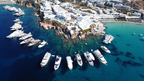 aerial drone, bird's eye view photo of luxury yachts docked near turquoise sea in paradise beach of psarou and platy gialos full of pool resorts and rocky seascape, mykonos island, cyclades, greece