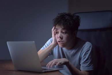 sleepy exhausted young asian man working late night at office desk with his laptop, his eyes are gonna closing and he is about to fall asleep, sleep deprivation and overtime overload working concept.