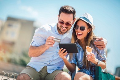 happy couple paying on line with credit card and digital tablet on the street