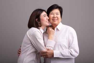 beautiful senior mom and her adult daughter are hugging, looking at camera and smiling
