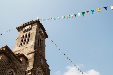 old catholic church tower with a clock, decorated with colorful flags. historical gothic style architecture in a town of nha trang, vietnam