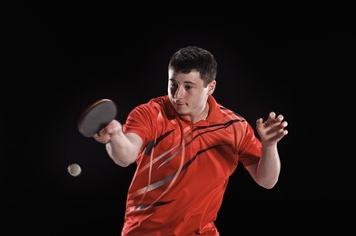 young man tennis-player in play on black background