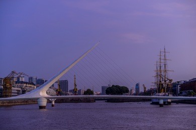 women's bridge in the financial district and port of buenos aires, argentina, at sunset with a sailboat behind it