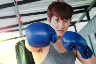 portrait of a young handsome asian man practicing boxing on a punching bag at the sport club