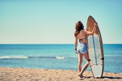 young surfer girl at the beach with her surfboard looking for the waves