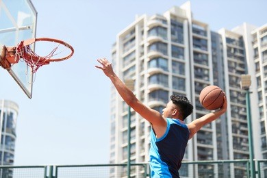young asian adult dunking basketball on outdoor court.