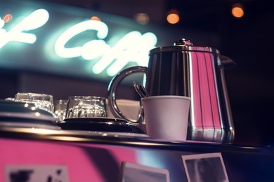 coffee or tea pot, cups, plates and glass glasses stand on the espresso machine, behind the neon inscription of coffee.