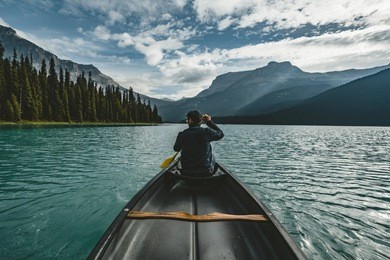 young man canoeing on emerald lake in the rocky mountains canada with canoe and mountains in the background blue water.