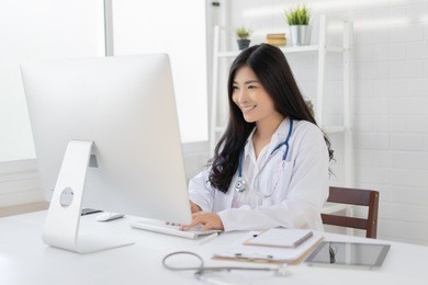 asian female doctor work at hospital office desk giving patient convenience online service advice, smiling write a prescription order medical with smartphone, health care, preventing disease concept.