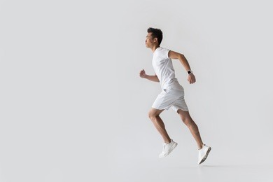 side view of young asian male athlete running on grey background 