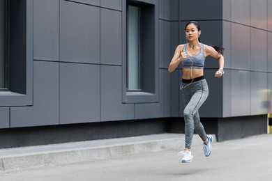 attractive young asian sportswoman in earphones running at city street