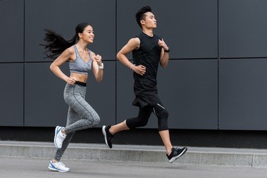 side view of asian sportsman and sportswoman running at city street 