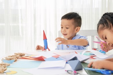 cute asian little boy playing with paper rocket while sitting in art class