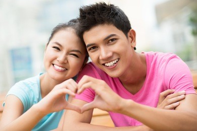 portrait of a guy and a girl forming a heart shape with their hands