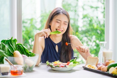 young asian woman happy eating healthy salad sitting on the table indoors. green healthy food concept.
