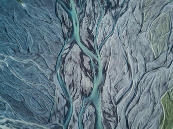 a drone shot from above on a green and blue metallic looking glacier river stream in iceland with repeating grey, beige and dark green patterns, textures and structures running from top to down