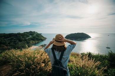 young asian woman traveler with backpack and hat looking view at view point look sunset at promthep cape phuket, thailand.
