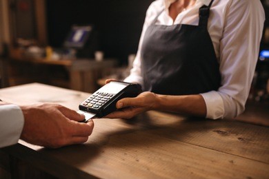 female bartender holding a credit card reader machine with male customer inserting the card in machine for payment.