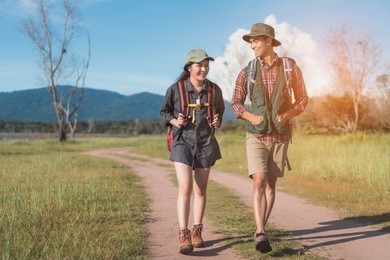 hikings couple asian walking travel together at forest for camping on holiday weekend talking about something on the go near river and mountain view.