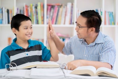 portrait of an asian male teacher doing high five with his student while studying together in the library