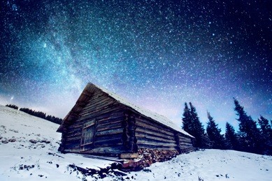 fantastic winter landscape glowing by stars light. the night sky with stars and the milky way. dramatic wintry scene with snowy wooden house and frozen fir tree. carpathian mountains, ukraine, europe.