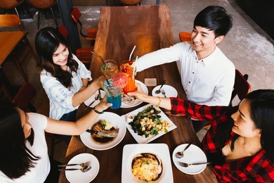 group of asian happy and smiling young man and women holding an alcoholic cocktail for toasting and celebrating in social party in restaurant - top view