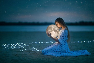 beautiful attractive girl on a night beach with sand and stars hugs the moon, artistic photography