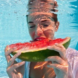 underwater woman eating a slice of watermelon in swimming pool.