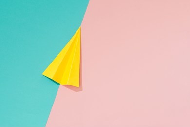 yellow paper airplane on pastel pink and blue background. minimal flat lay school concept.