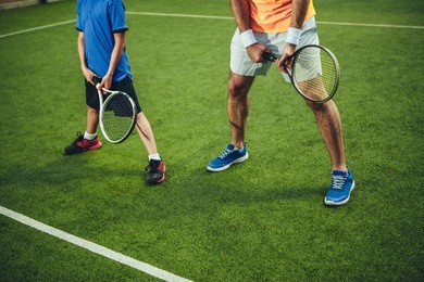man and child playing tennis while situating on green field for game outdoor. they wearing modern trainers