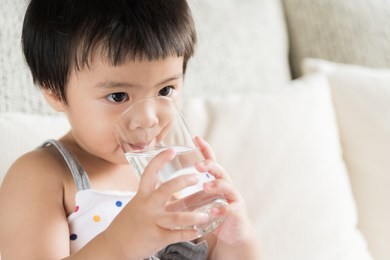 cute little girl drinking water on sofa at home. health care concept.