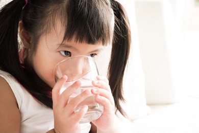 cute little girl drinking water on sofa at home. health care concept.