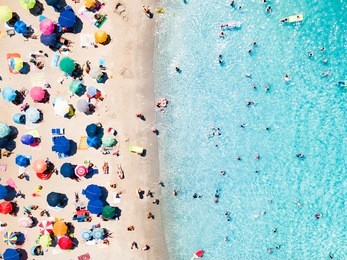 view from above, aerial view of an emerald and transparent mediterranean sea with a white beach full of beach umbrellas and tourists who relax and swim. costa smeralda, sardinia, italy.