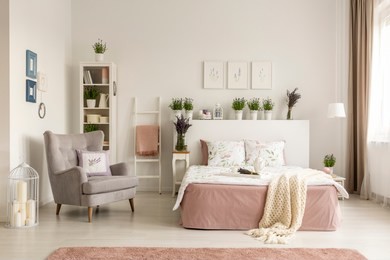 real photo of a feminine bedroom interior with a comfy armchair, bed, plants and shelf