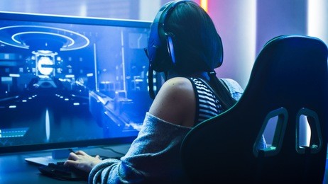 shot of the beautiful pro gamer girl playing in first-person shooter online video game on her personal computer. casual cute geek wearing glasses and headset. neon room. esport cyber games internet