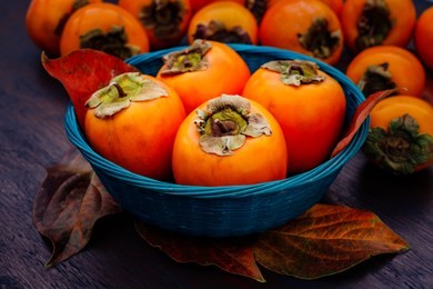 ripe orange persimmon fruit and persimmon leaves in a blue basket on a brown wooden table