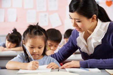 teacher helping student working at desk in chinese school classroom