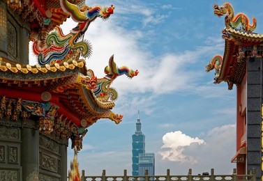 view of the colorful roof of an archway to a taiwanese temple with delicate & fancy decorations of sculptures in traditional mosaic art & the modern buildings in background in taipei city, taiwan asia