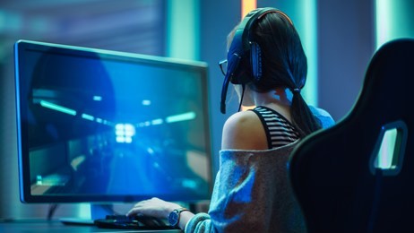 shot of the beautiful pro gamer girl playing in fps video game on her personal computer, casual cute geek wearing glasses and headset. neon room. online cyber games internet championship event.
