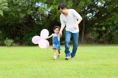 asian father and daughter are playing the balloons and they running and laughing together with fully happy moment in the park, concept of outdoor activity in family lifestyle.