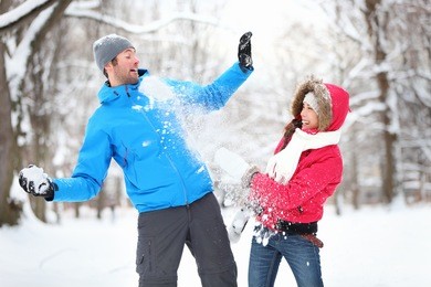 carefree happy young couple having fun together in snow in winter woodland throwing snowballs at each other during a mock fight