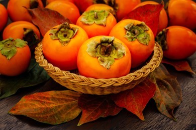 persimmon fruits and persimmon  leaves in basket on wooden background