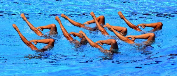synchronized swimmers point up out of the water in action. synchronized swimmers legs movement. synchronized swimming team performing a synchronized routine of elaborate moves in the water.