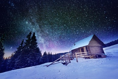 fantastic winter landscape glowing by stars light. the night sky with stars and the milky way. dramatic wintry scene with snowy wooden house and frozen fir tree. carpathian mountains, ukraine, europe.