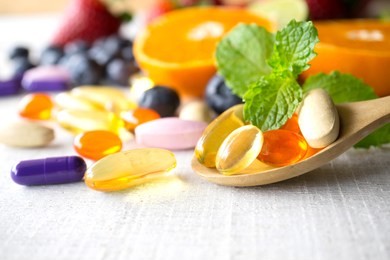 colorful pills and capsules in wooden spoon with fresh fruits.vitamins and supplement from fruits concept.