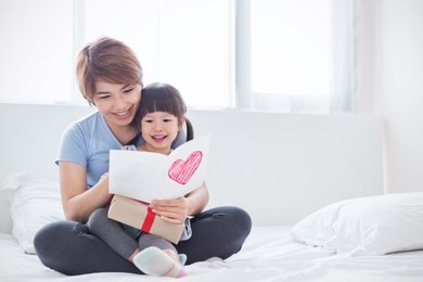 little asian girl daughter congratulate mommy giving a surprise card and gift box. family holiday mother and girl celebrate together. love lifestyle mother’s day background concept